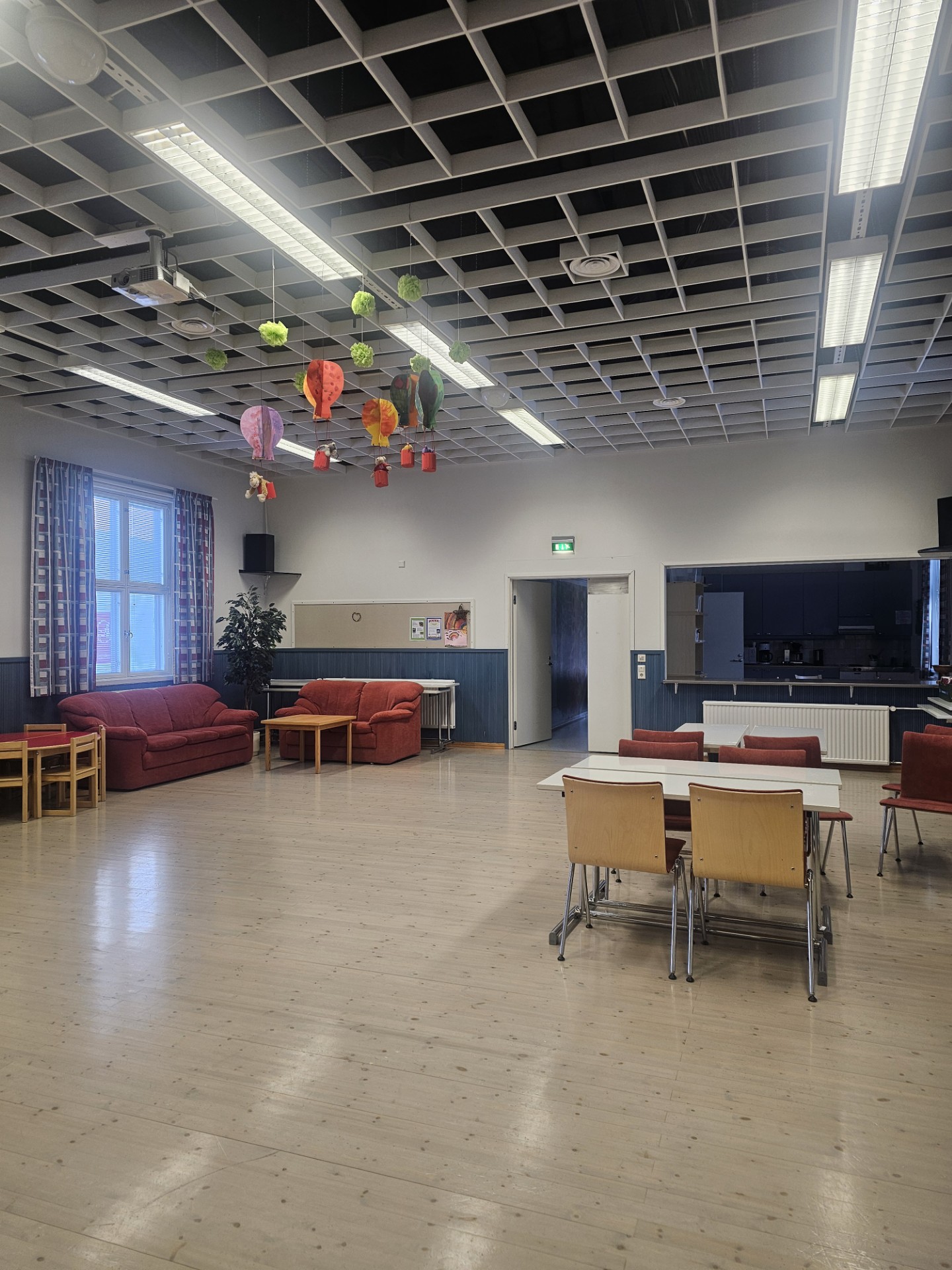 Nuorisotila Kuvassa nuorisotila ja sen varustelua. Sali, jossa pöytiä ja tuoleja. Tuoleja pinottain seinustalla. Taustalla näkyy pieni tarjoilukeittiö. Katosta riippuu kerholaisten taideteoksia: pahvisia kuumailmapalloja eri väreissä.