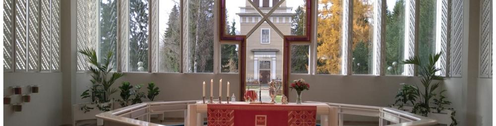 Lieksan kirkon alttariosa puettuna punaisiin kirkkotekstiileihin. Ikkunoista näkyy kirkkopuisto ja kellotapuli