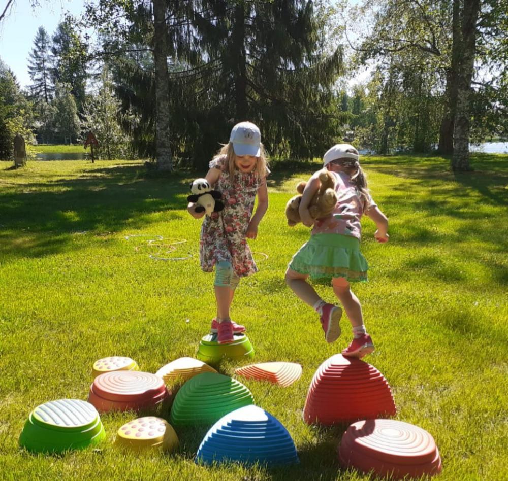 Kaksi tyttöä kävelee värikkäitä muovisia leikkikiviä pitkin
