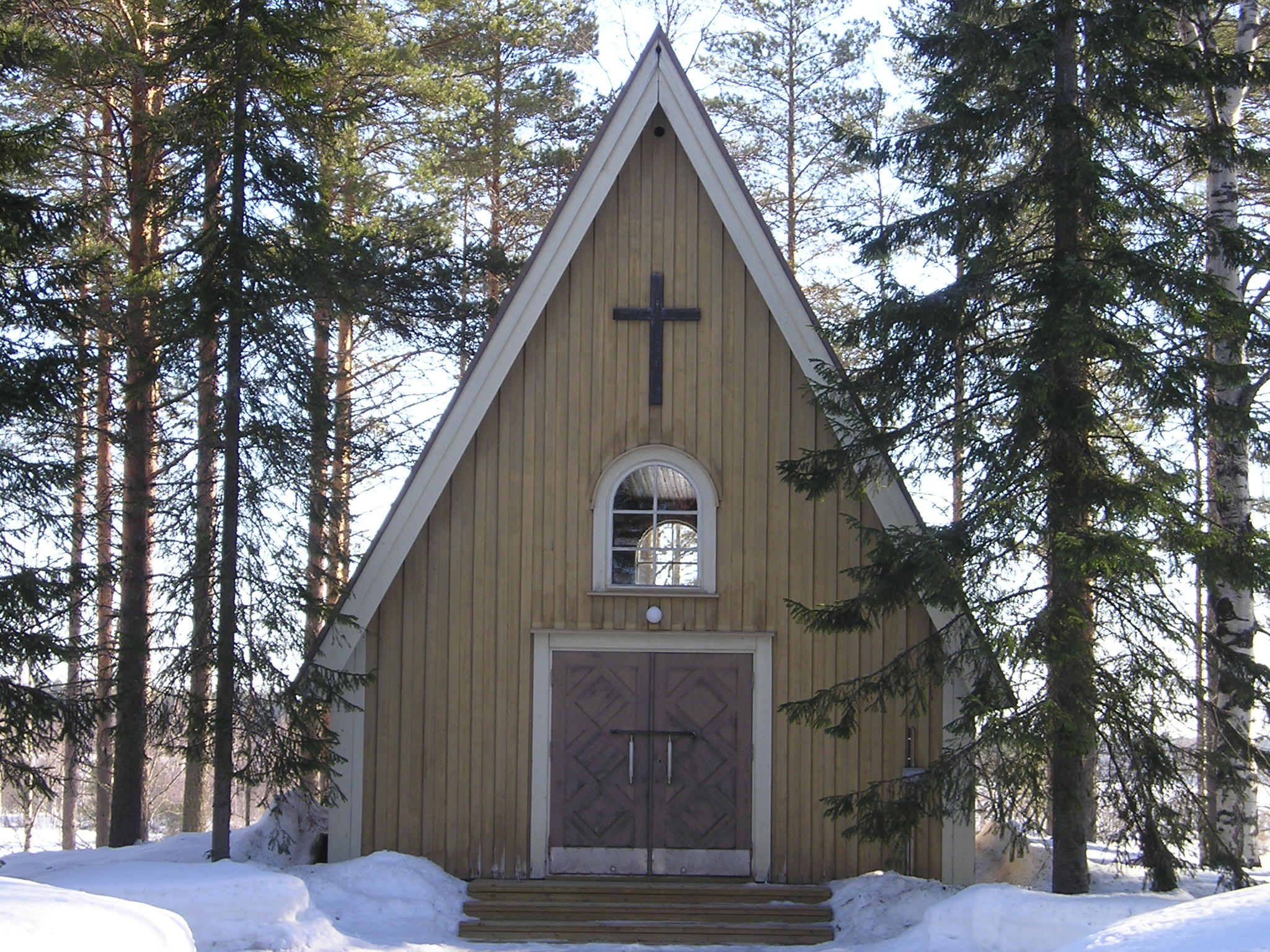 Jyrkkäharjainen rakennus puiden ympäröimänä.