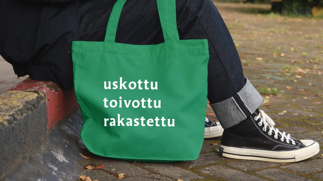 Henkilö kuljettaa vihreää kestokassia, Kuva rajautuu henkilön jalkoihin